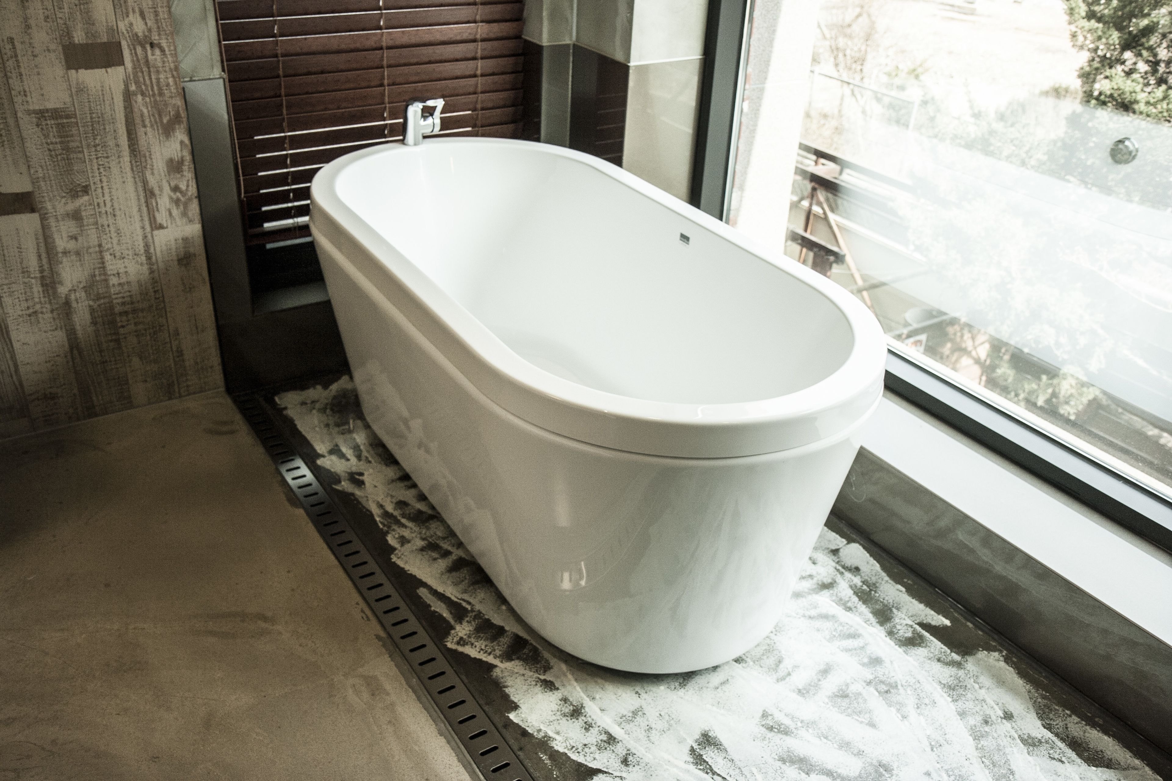 A modern bathroom with a freestanding bathtub, a window with a view of the street, and a shower area with a drain.
