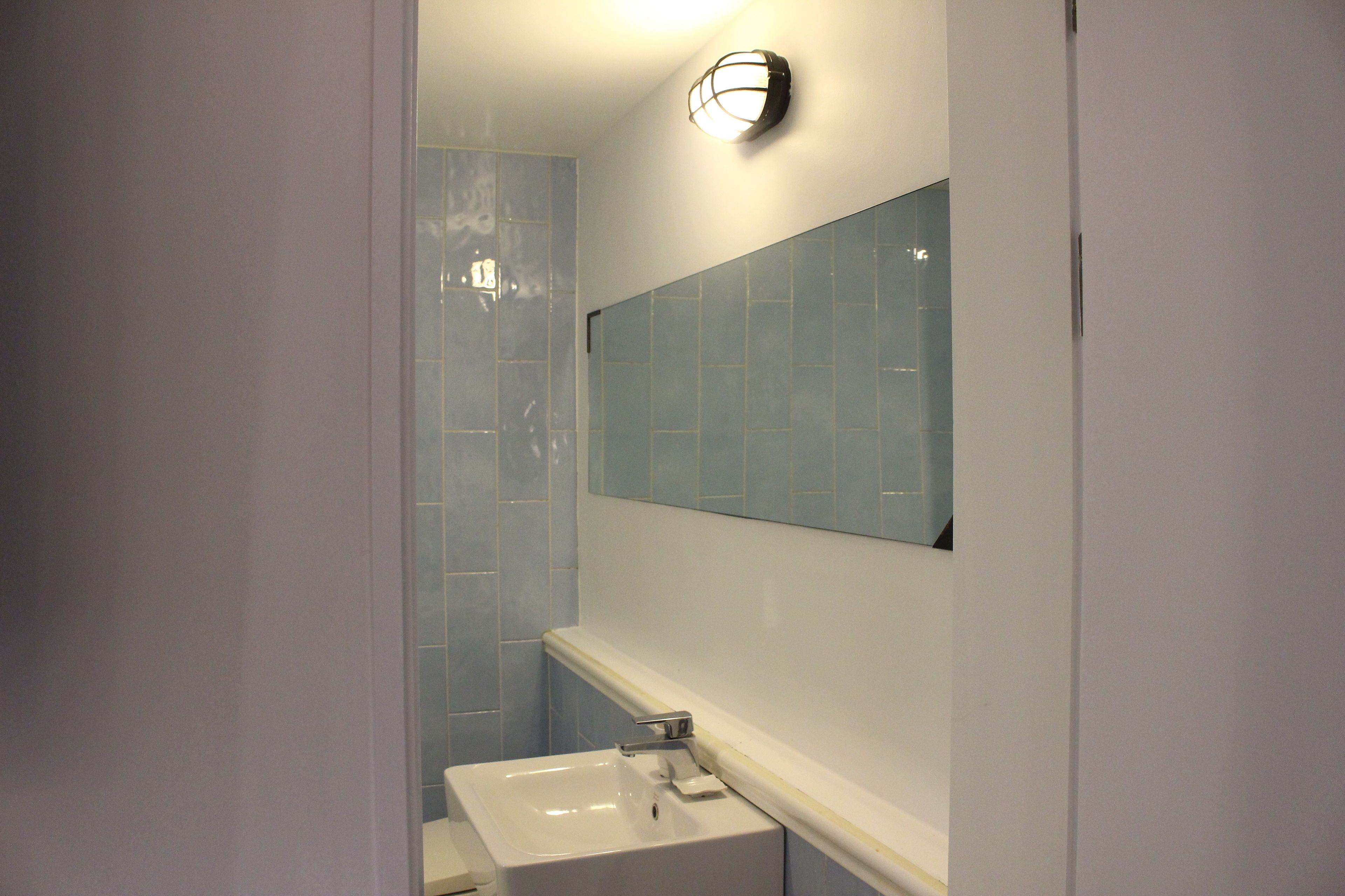 A bathroom with a white sink, a mirror, and light blue tiles.