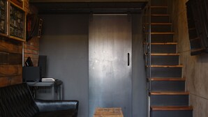 Une pièce avec un escalier en bois, un canapé en cuir, une petite commode en bois et une porte dotée d’une poignée en métal.