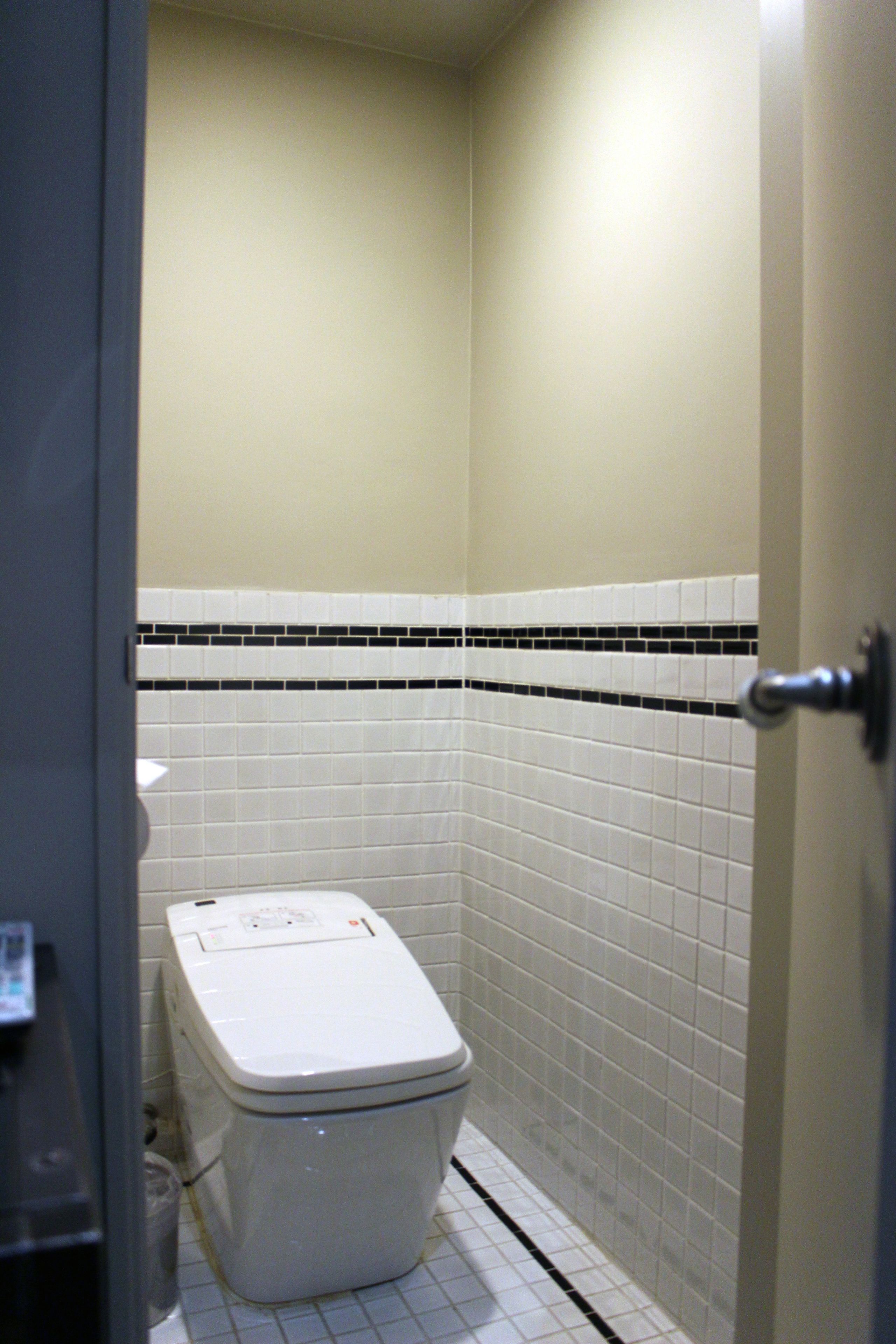 A small, narrow bathroom with a toilet, tiled walls, and a door.