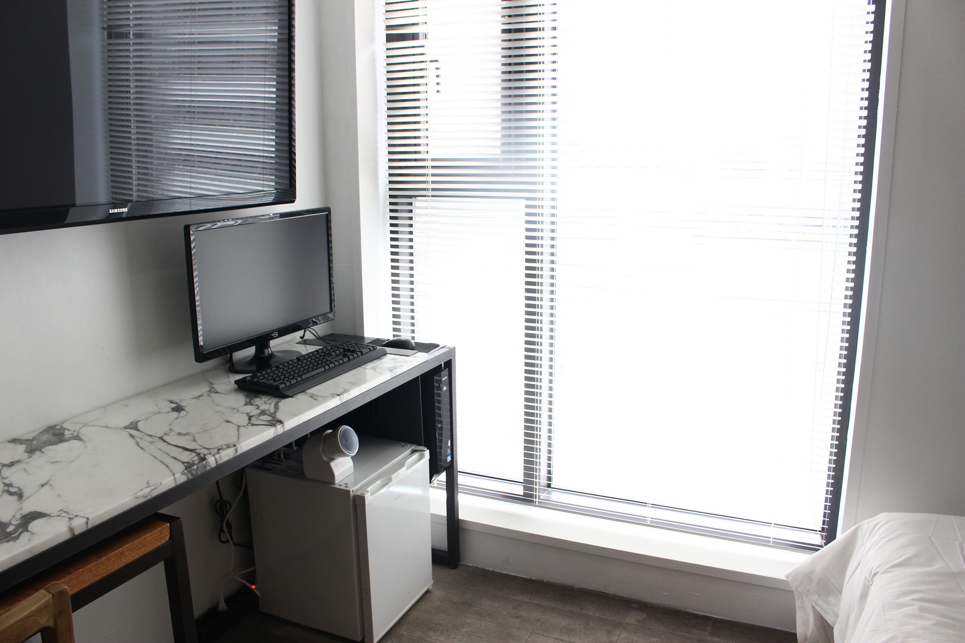 A modern office space with a marble desk, a computer monitor, keyboard, and a small white speaker.