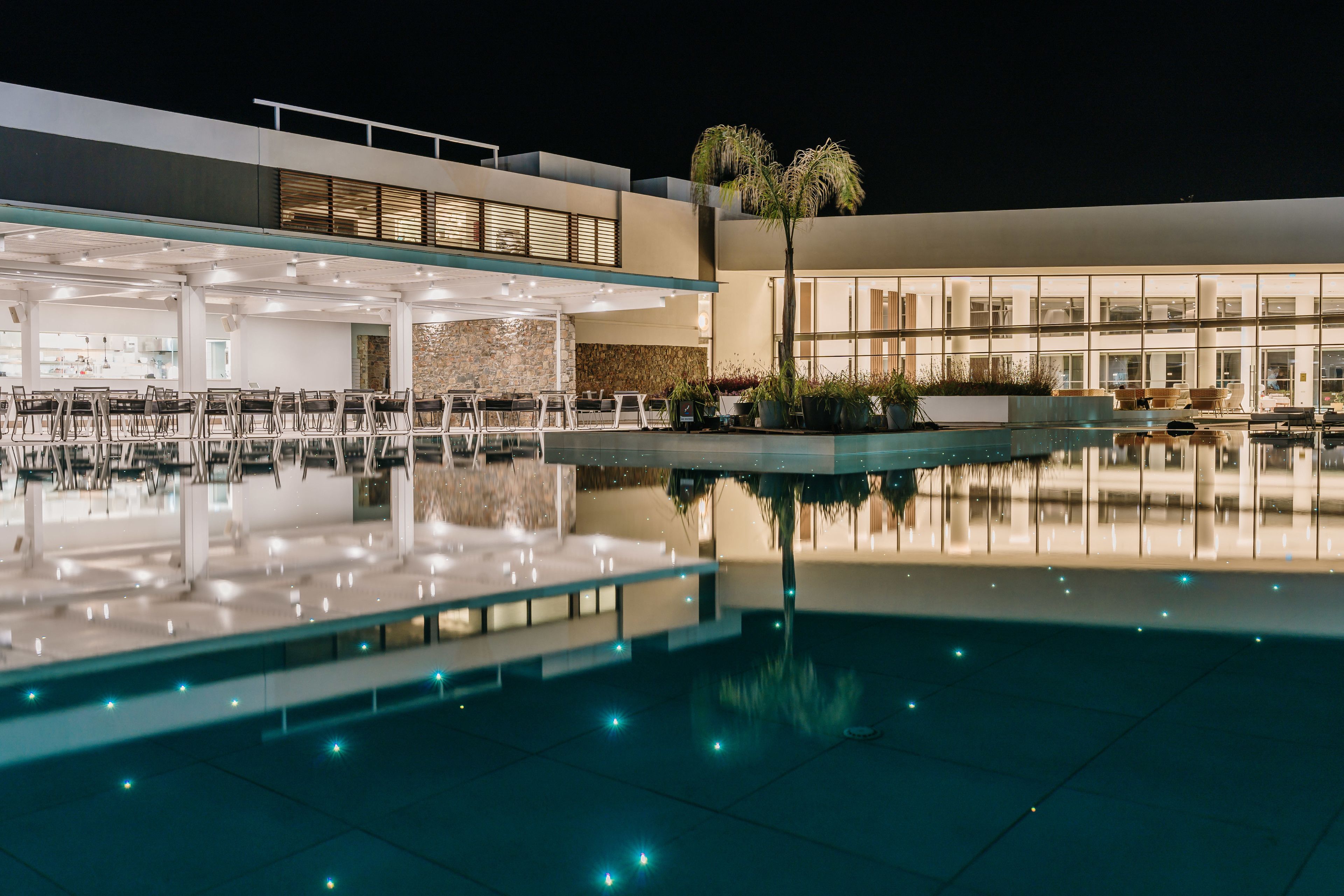 Un hôtel moderne doté d’une piscine, d’un espace extérieur aménagé et d’une façade bien éclairée.