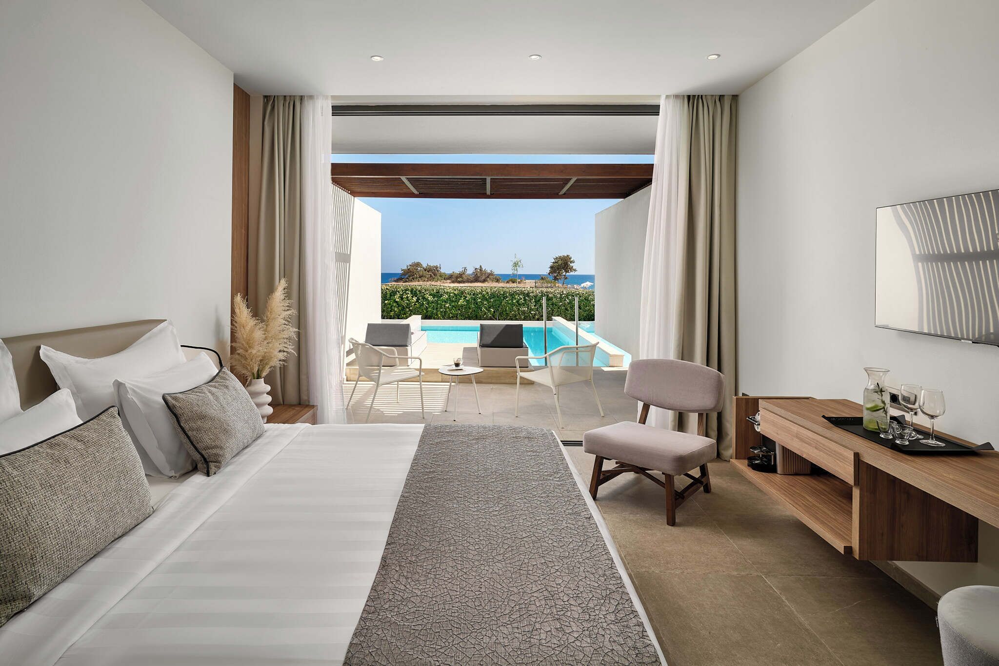 Una camera da letto moderna con un letto grande, una scrivania in legno e vista su una piscina e del verde.