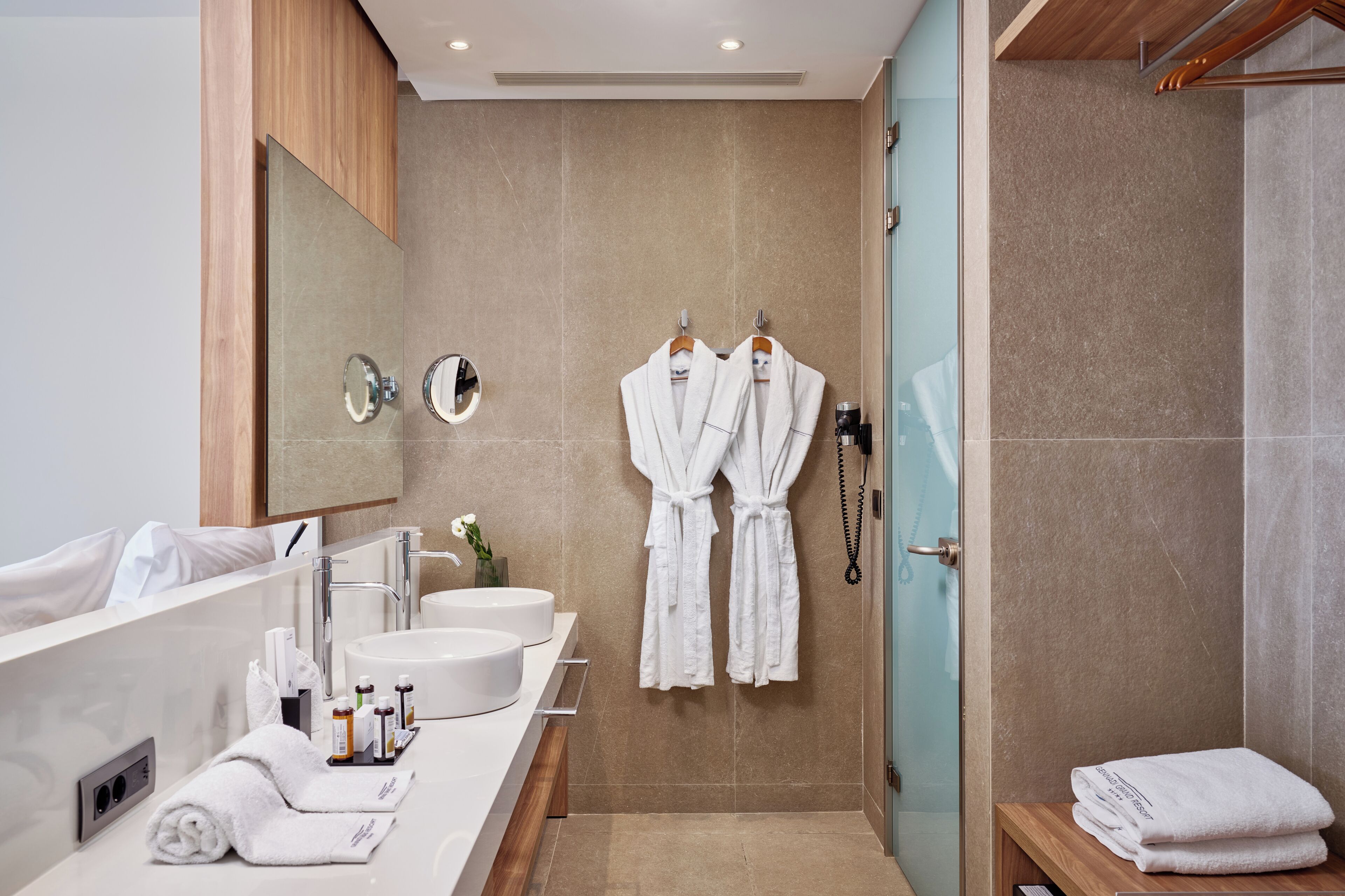A modern bathroom with a large mirror, two sinks, and a shower area.