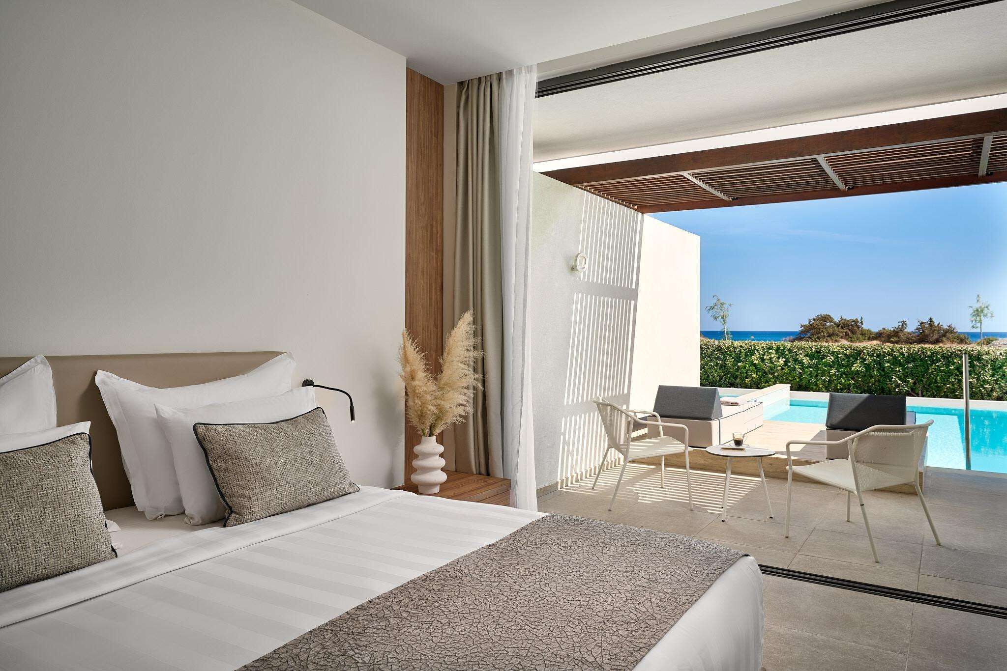 Una habitación de hotel moderna con cama, vista a la piscina y mobiliario exterior.