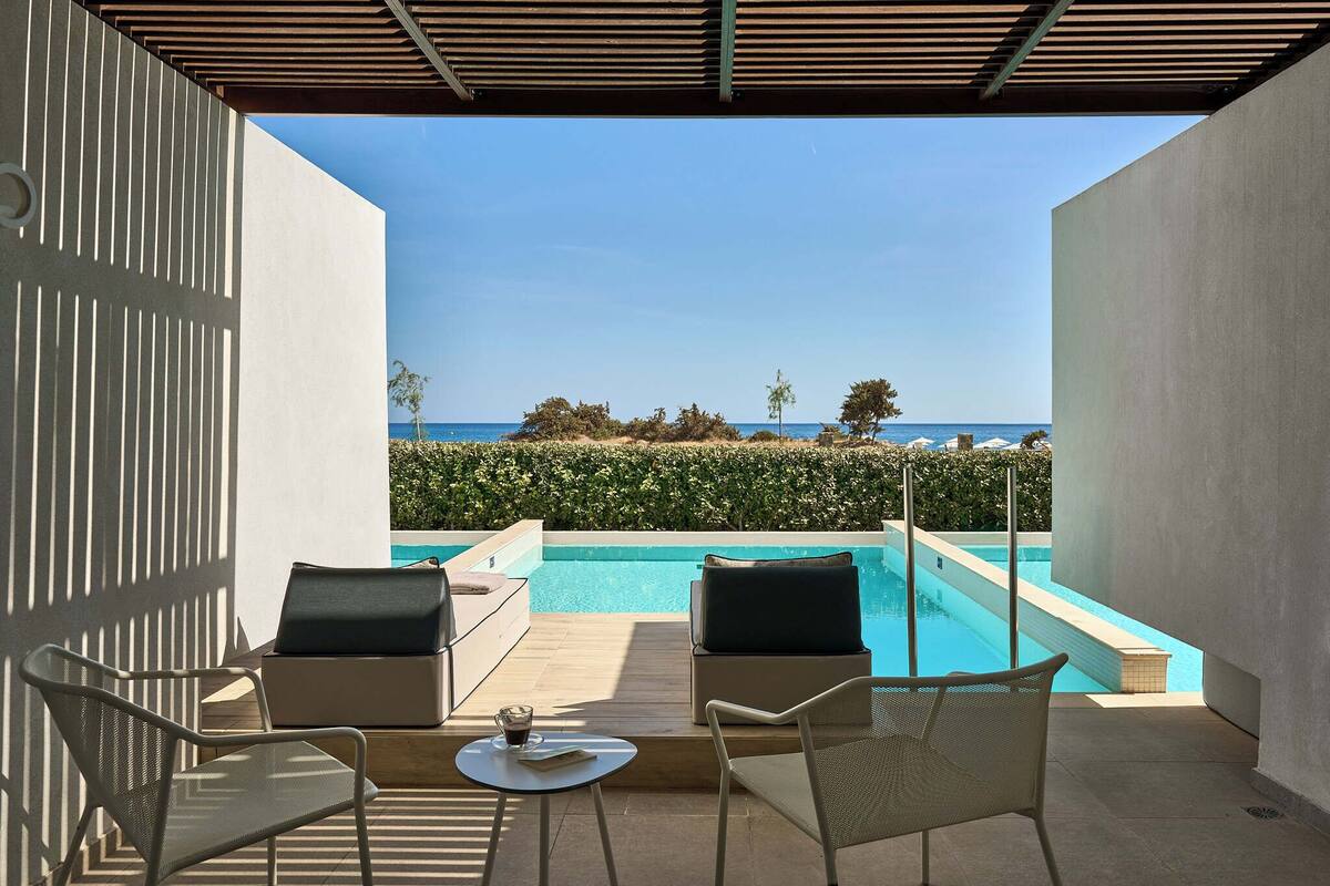 Ein moderner Außenbereich mit Pool, der auf einen wolkenlosen, blauen Himmel und eine ferne Meerblick blickt.