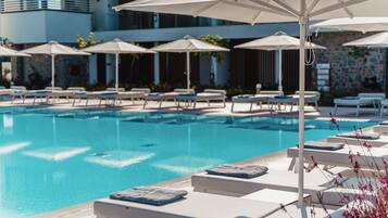 A pool area with lounge chairs and umbrellas, a clear blue pool, and a stone wall in the background.