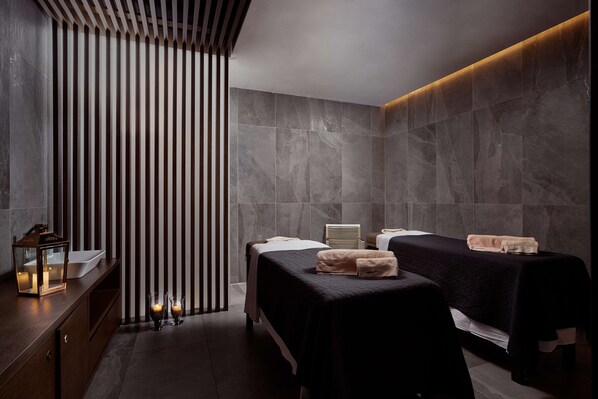 A modern spa room with two treatment beds, a wooden panel wall, and a marble-tiled wall. - Gennadi Grand Resort (Rhodes)