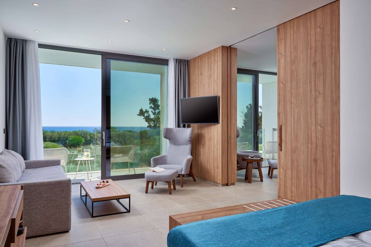 Ein modernes Hotelzimmer mit einem großen Bett, einer Couch, einem Sessel, einem kleinen Tisch und einem an der Wand befestigten Fernseher.