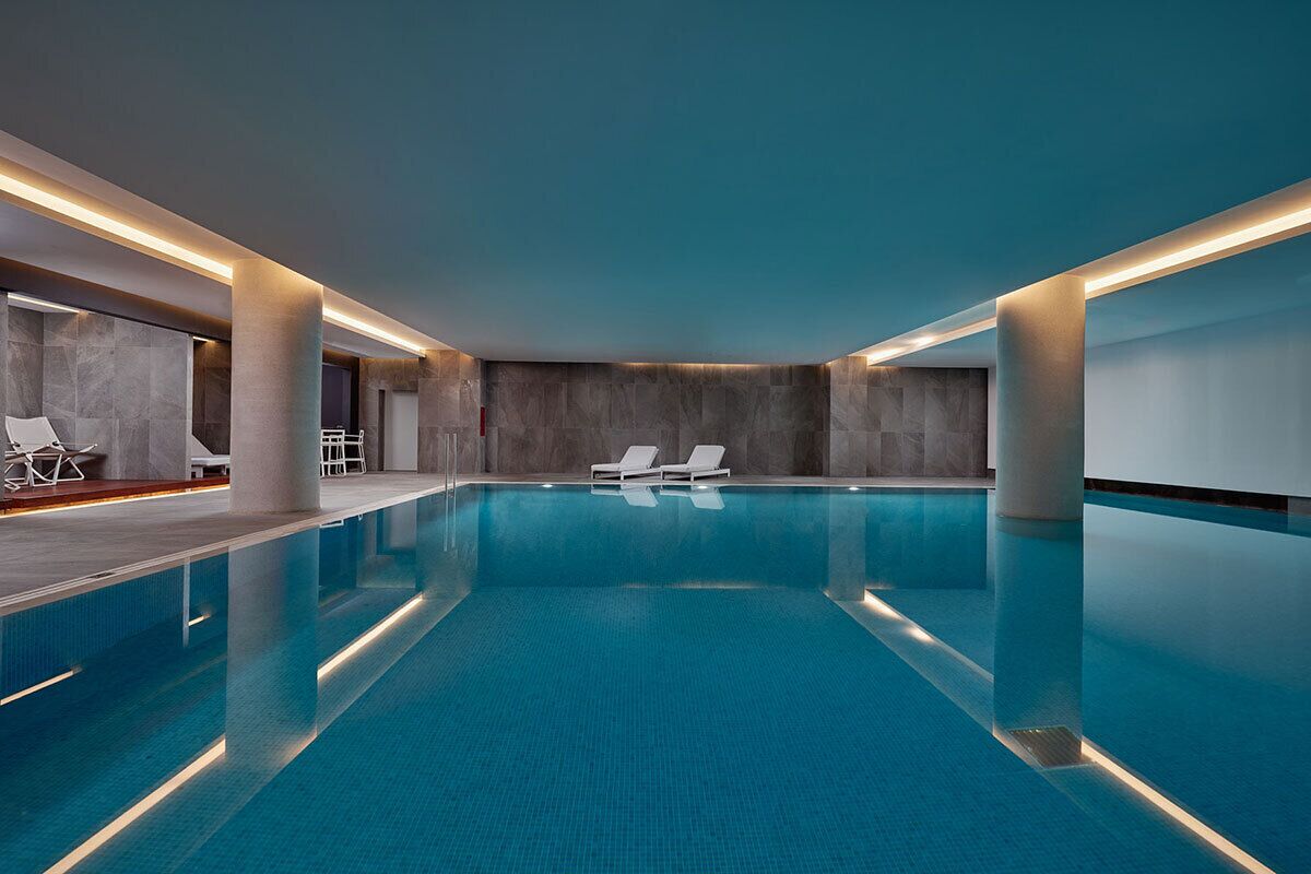 A modern indoor swimming pool with clear blue water, lounge chairs, and a minimalist design.