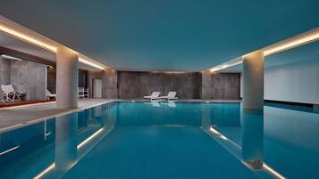 A modern indoor swimming pool with clear blue water, lounge chairs, and a minimalist design.