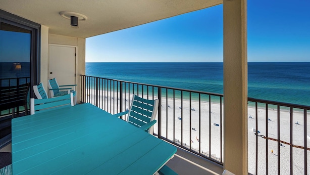A balcony with a view of the ocean, a table, and chairs.