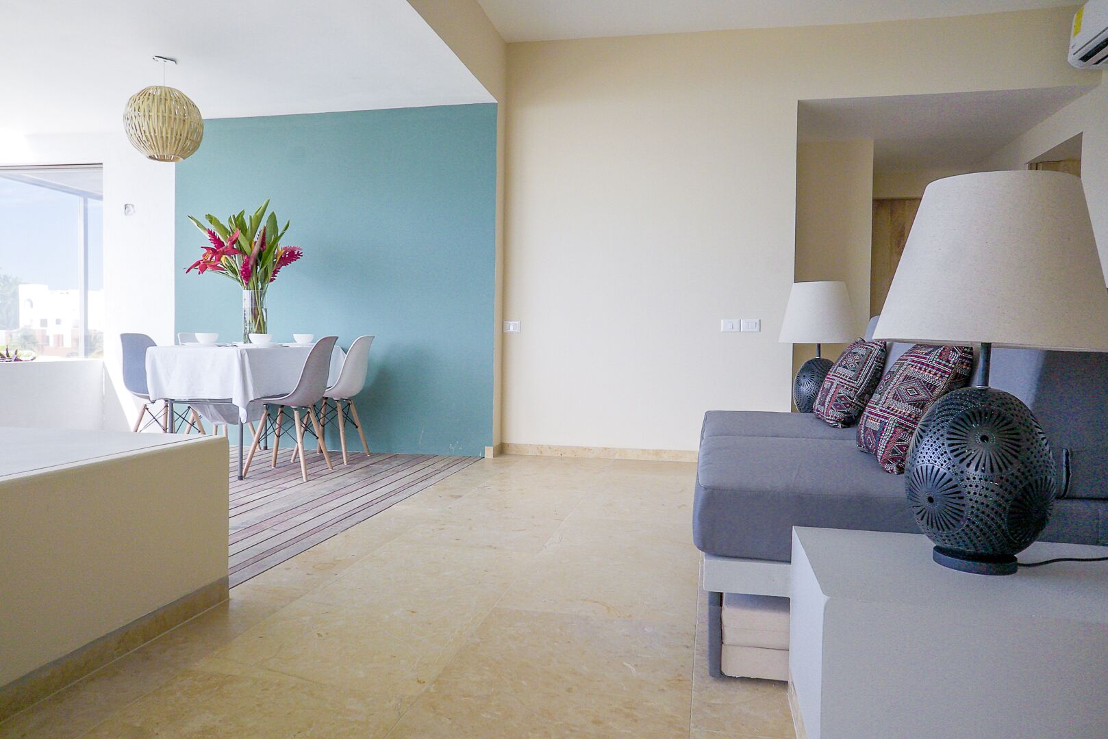 A modern living room with a grey sofa, a dining table with chairs, and a vase of flowers.