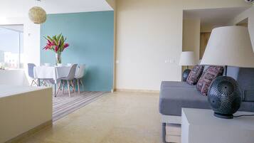 A modern living room with a grey sofa, a dining table with chairs, and a vase of flowers.