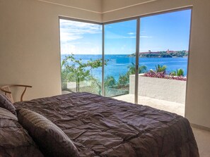 A bedroom with a large bed, a view of the sea, and a balcony with plants.