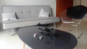 A modern living room with a grey sofa, a black coffee table with decorative items, and a wireframe chair. - Geo Maisonette Lagonissi (Saronikos)