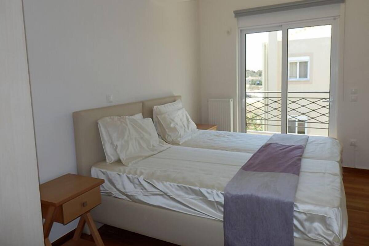Ein Schlafzimmer mit zwei Betten, einem hölzernen Nachttisch und Blick durch eine Schiebetür auf einen Balkon.