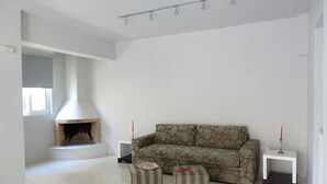 A living room with a fireplace, a sofa, two ottomans, and a small white side table. - Geo Maisonette Lagonissi (Saronikos)