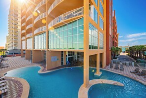 A hotel with a pool area, multiple balconies, and a clear sky.