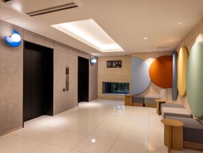 A modern lobby with a glass ceiling, elevators, a reception desk, and a wall with abstract art. - Ibis budget Osaka Umeda (Osaka)