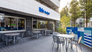 Un área de estar al aire libre con mesas y sillas frente a un edificio con un letrero que dice "ibis budget".