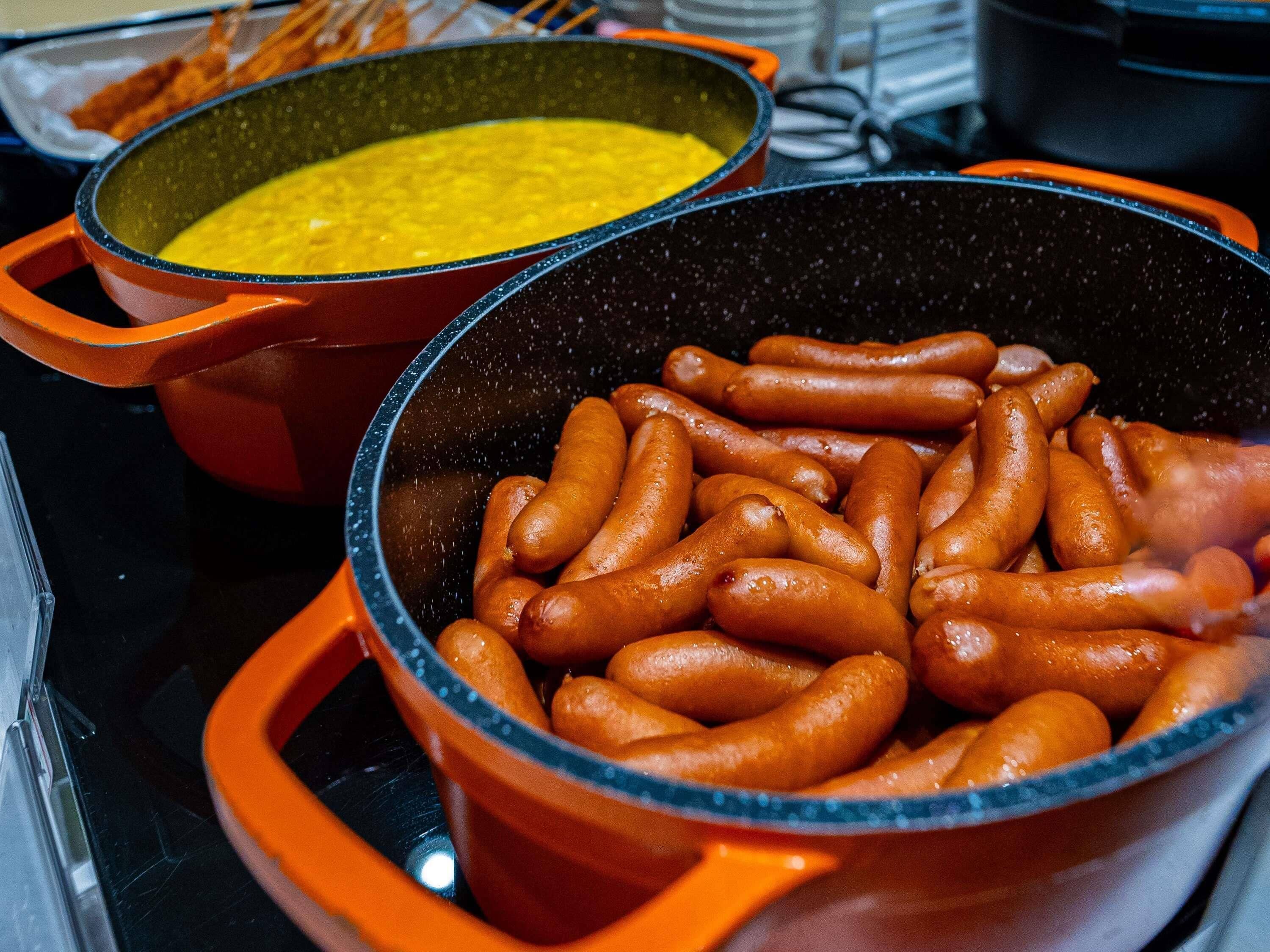 Two pots on a stove, one with sausages and the other with a yellow mixture.