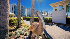 Eine Vogel-Skulptur in einer angelegten Grünfläche mit Palmen und einem Gebäude im Hintergrund.