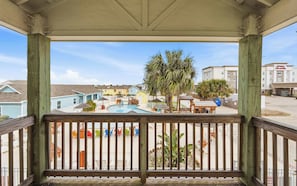 A pool area with lounge chairs and umbrellas, a wooden deck with railings, and a view of a hotel building in the background. - Pool, Near Beach & 4BR Family Retreat - Sailfish (Port Aransas)