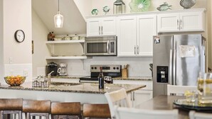Een moderne keuken met witte kasten, roestvrijstalen apparatuur, een granieten werkblad en een eethoek met houten stoelen.