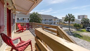 A wooden deck with red Adirondack chairs and a wooden bench, overlooking a beachfront property with a white building and palm trees. - Prime Beach/Lagoon Location!  Walk to beach and restaurants! (Gulf Shores)