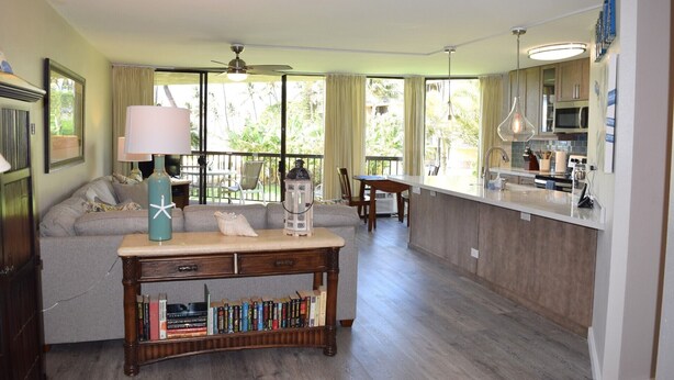 Amplia sala de estar con un sofá, una mesa de centro con libros, una mesa de comedor y una cocina con microondas y lavaplatos.