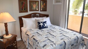 Una cama bien hecha con colcha, una lámpara de noche y una mesita de noche con un control remoto.