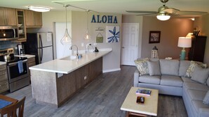 Una cocina moderna con una isla central, un comedor con mesa de madera y una sala de estar con sofá gris.