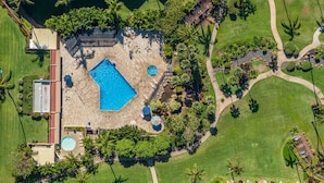 An aerial view of a resort with a large swimming pool, multiple smaller pools, and a well-maintained garden with palm trees. - Beautiful garden view condo with tropical decor (Kihei)