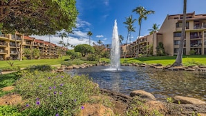 A hotel courtyard with a central fountain, surrounded by lush greenery and palm trees. - Beautiful garden view condo with tropical decor (Kihei)