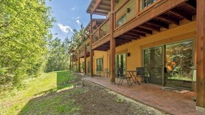 A wooden cabin with a patio area, large windows, and a view of the surrounding forest.
