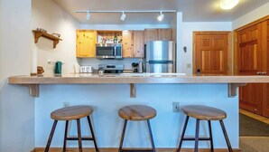 A modern kitchen with wooden cabinets, a stainless steel refrigerator, a microwave, and a bar area with stools.