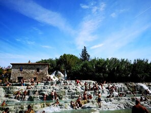 A stone building with a tiled roof, surrounded by lush greenery and a clear blue sky. - La Biocca (Manciano)