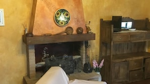 A cozy living room with a fireplace, a covered sofa, and a wooden cabinet. - La Biocca (Manciano)