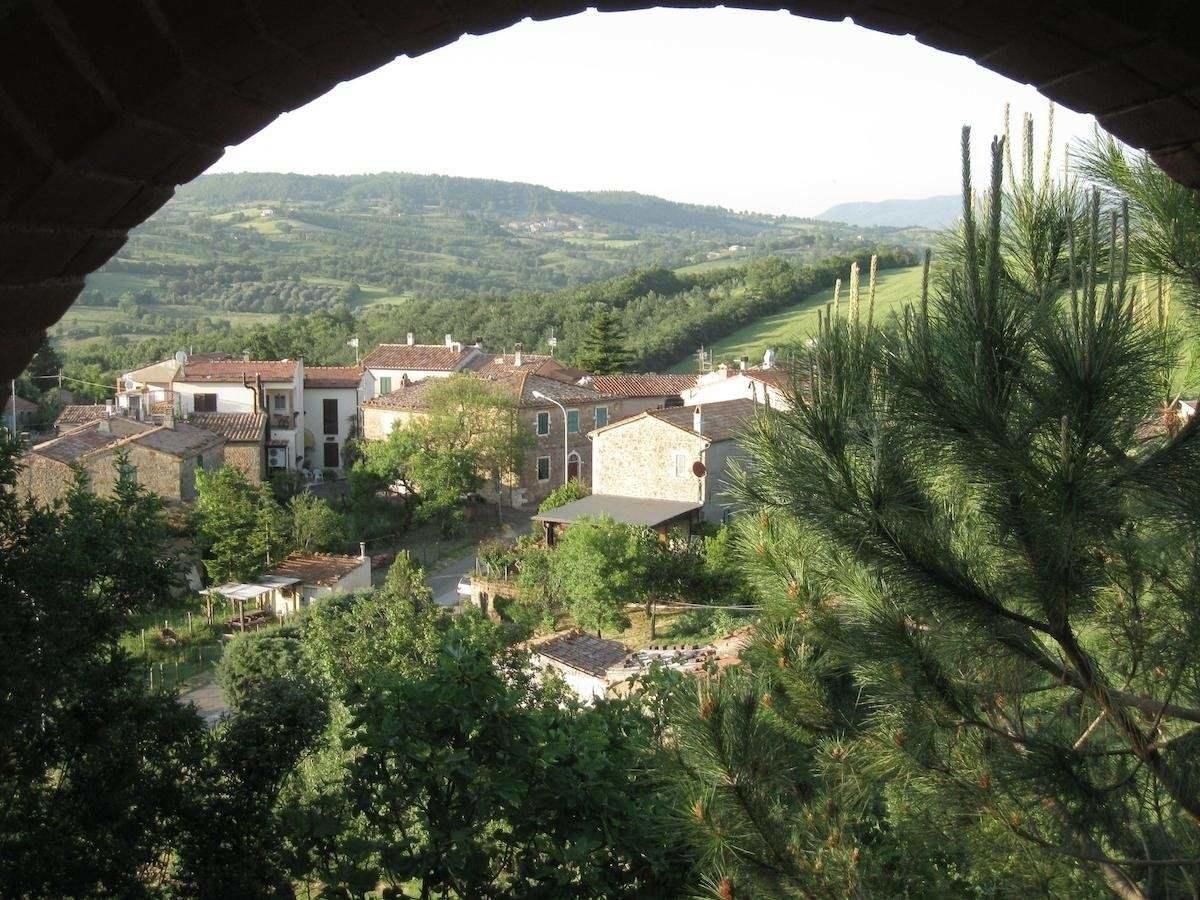 A view of a village through an archway, featuring traditional buildings and lush greenery.