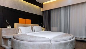 A round bed with a headboard, bedside tables, and a large window with curtains. - Gold Crest Hotel - Mwanza (Mwanza)