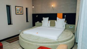 Una habitación de hotel moderna con una cama grande, una mesita de noche y una zona de estar circular.