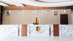 A hotel reception desk with a marble design, a receptionist, and clocks on the wall. - Gold Crest Hotel - Mwanza (Mwanza)