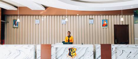 A hotel reception desk with a marble design, a receptionist, and clocks on the wall.