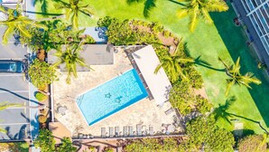 Vista aérea de un resort con piscina rodeada de palmeras y un estacionamiento.