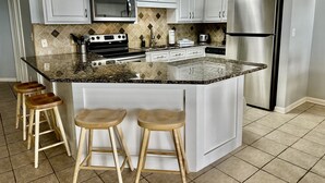 Una cocina moderna con armarios blancos, un refrigerador de acero inoxidable, un microondas y una estufa. Hay dos taburetes de madera en la isla.