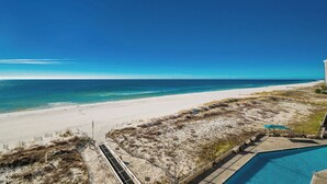 A beach view with a pool and a sandy area with sparse vegetation.