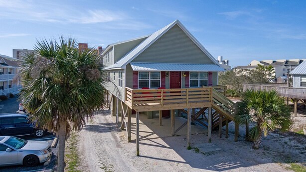 Une maison située en bord de mer, dotée d’une terrasse en bois et d’une porte rouge.