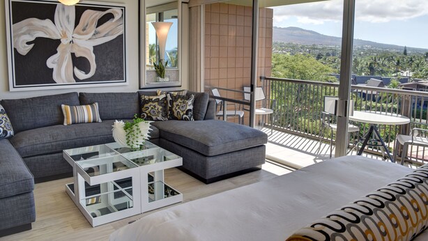 A modern living room with a gray sofa, a glass coffee table, and a balcony with a view of a cityscape and mountains. - Oceanfront Condo at the Mana Kai Maui, Luxurious, Designer Remodeled (Kihei)