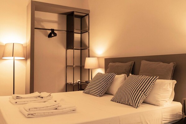 Habitación de hotel con una cama bien hecha, dos lámparas de noche, un cabecero y un estante de pared.